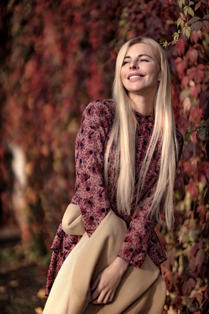 Девушка в розовом платье в красных листьях лозы дикого винограда счастливо улыбается