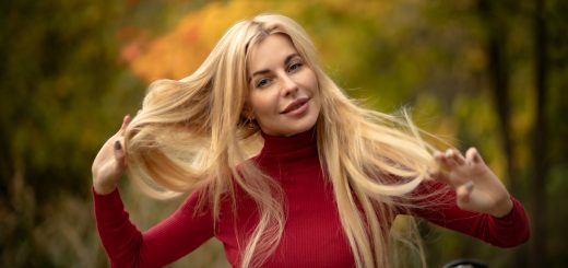 Девушка блондинка в красном осенью на природе поправляет волосы