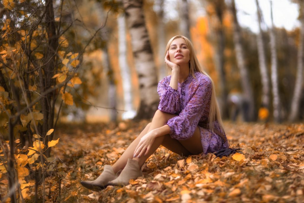Девушка сидит на пожелтевшей листве осенью в парке