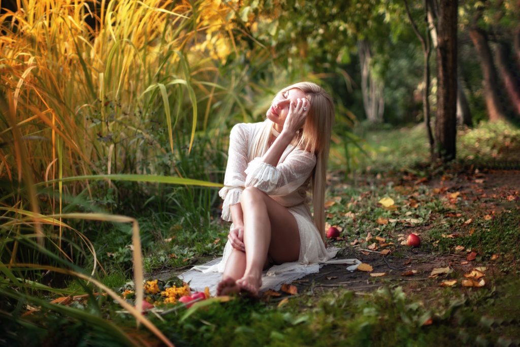 Девушка в светлом платье сидит на осенней траве возле камышей