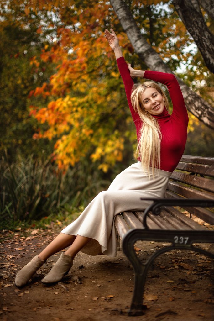 Девушка в красном на лавочке в осеннем парке счастливо улыбается