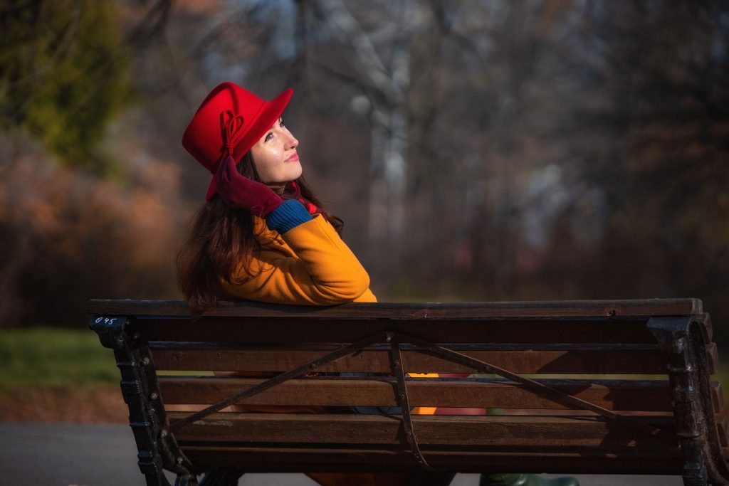Девушка в красной шляпе на лавочке радуется осеннему солнцу