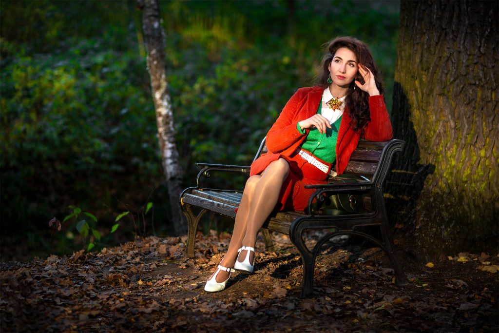 Девушка на скамейке в красном костюме мечтает в осеннем парке