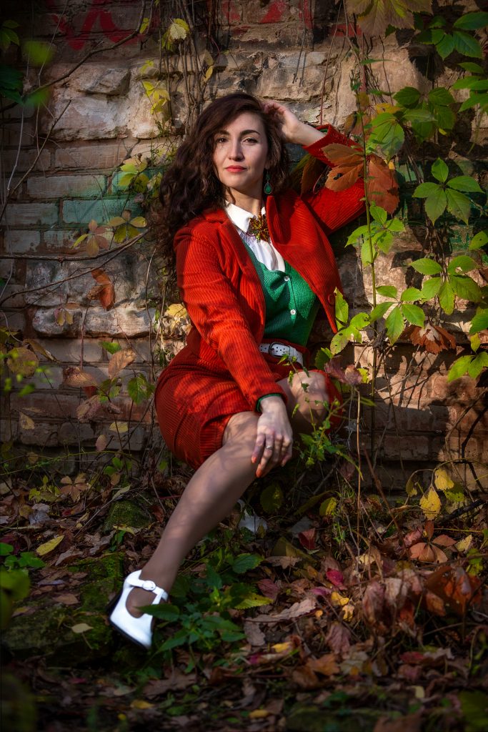 Девушка в красном костюме сидит возле стены с красивой осенней листвой