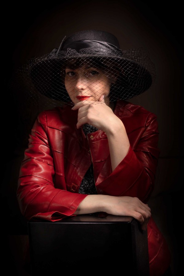 Дама в черной шляпе и красной куртке на тёмном фоне