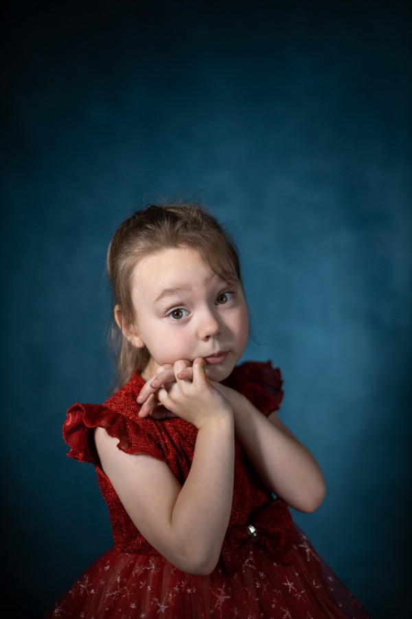 Маленькая девочка в красном платье мило сложила ладошки возле лица