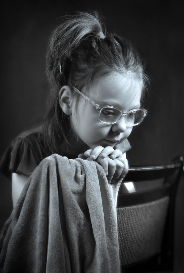 Девочка в очках грустит сидя на стуле черно-белый портрет
