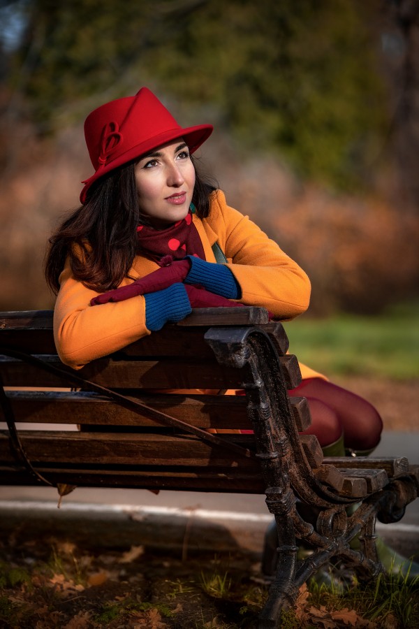 Девушка на лавочке в красной шляпе осенью радуется солнечном у дню