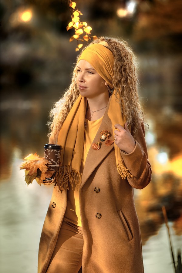 Девушка в желтом пальто осенью в парке пьёт кофе