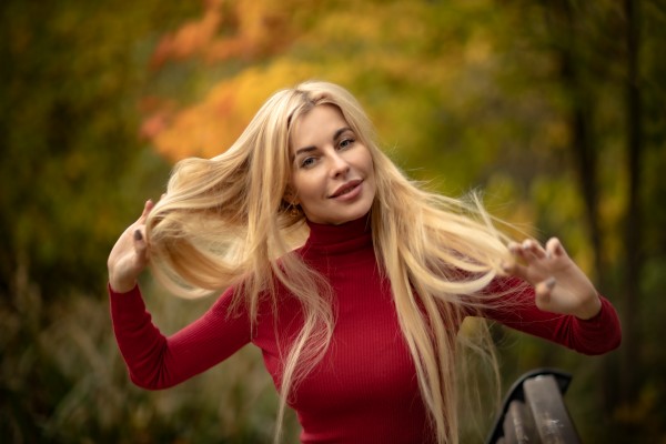 Девушка блондинка в красном осенью на природе поправляет волосы