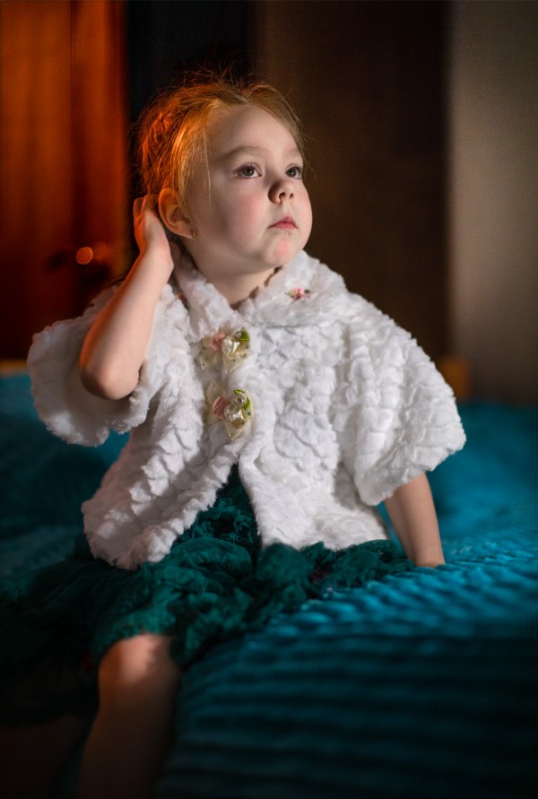 Маленькая девочка в белой кофте поправляет волосы