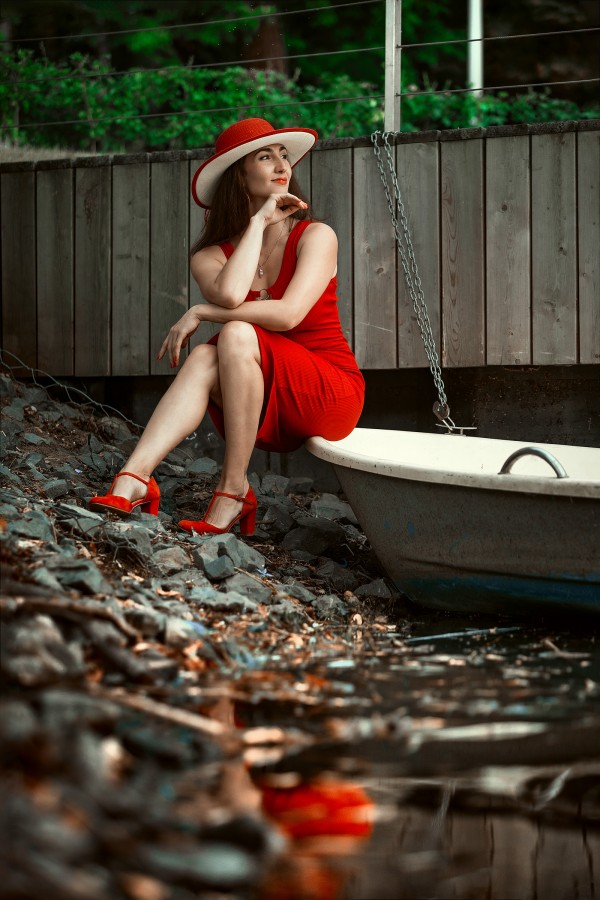 Девушка на лодке в красном платье мечтательно смотрит вдаль