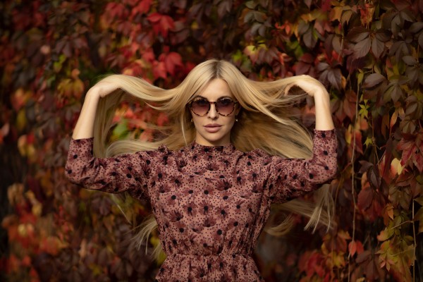 Девушка блондинка в солнечных очках возле красной лозы дикого винограда