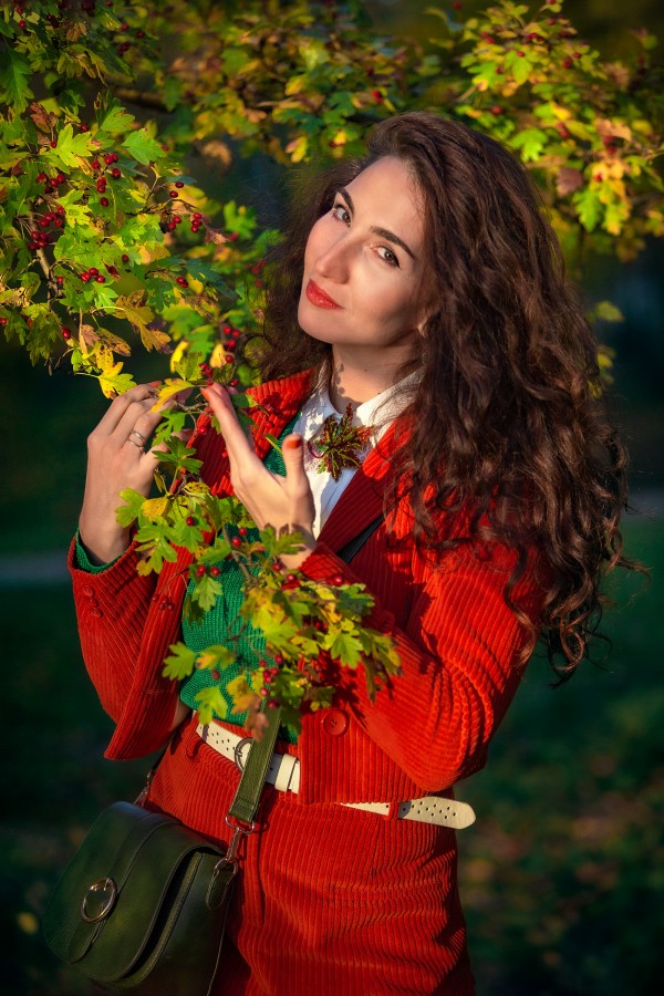 Девушка в красном загадочно смотрит возле осенней листвы дерева